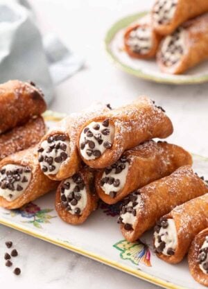 A platter with a stack of cannoli with a plate of three more in the background.