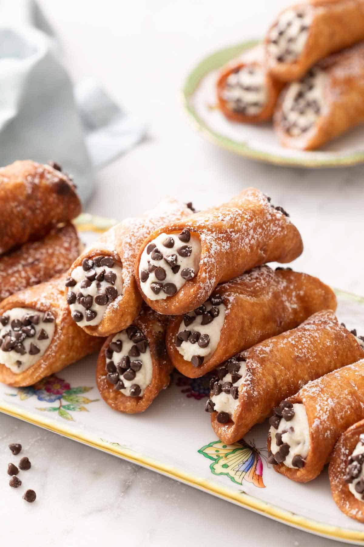 A platter with a stack of cannoli with a plate of three more in the background.