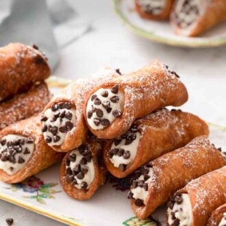 Pinterest graphic of a platter of cannoli topped with powdered sugar and filled with chocolate chips.