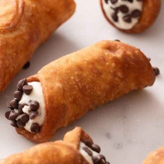 Multiple cannoli with chocolate chips on a marble surface.