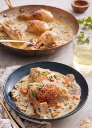 A plate with a serving of chicken fricassée with a skillet with more in the background.