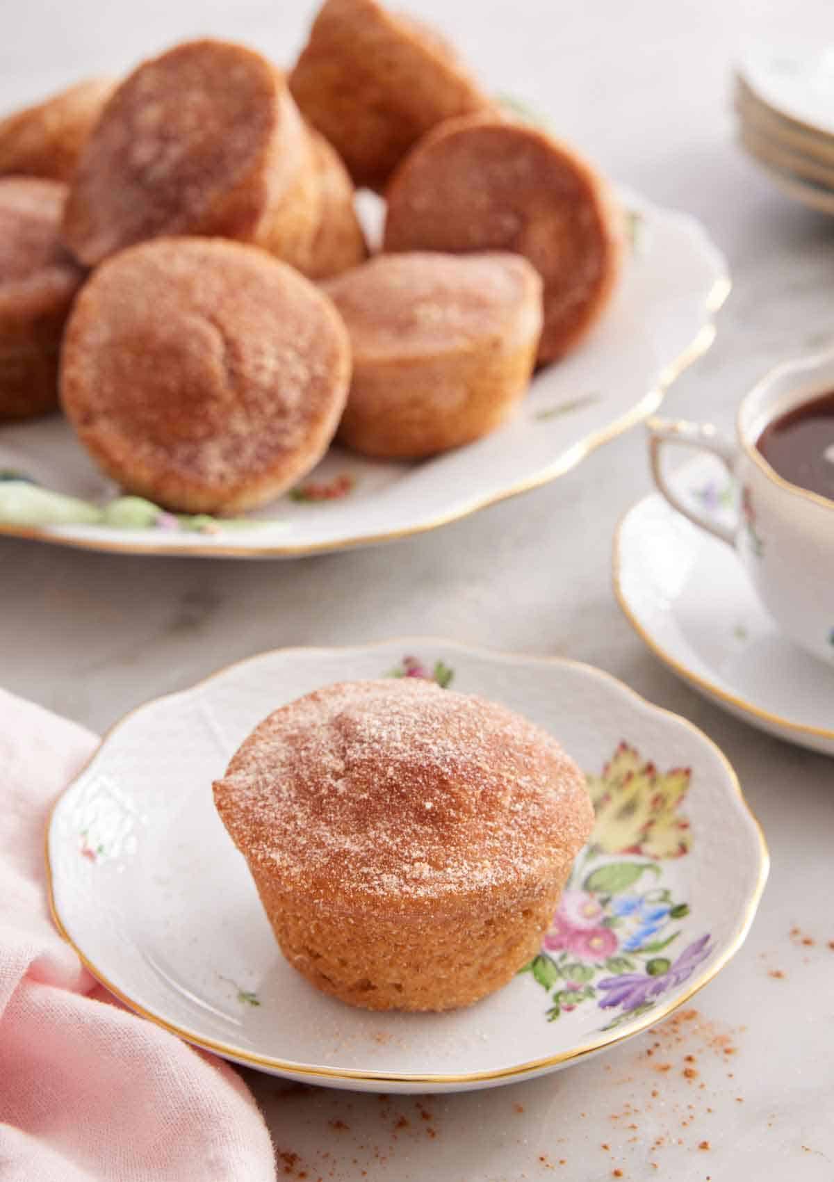 A plate with a cinnamon muffin with a platter in the back along with coffee.