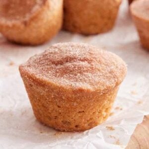 A cinnamon muffin on a wooden board lined with parchment with more muffins in the back.