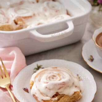 Pinterest graphic of a plate with a cinnamon roll on a plate with a baking dish with more cinnamon rolls in the background.