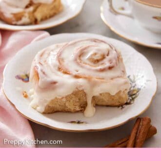 Pinterest graphic of two plates with cinnamon rolls and a cup of coffee in the background with some flowers and a book.