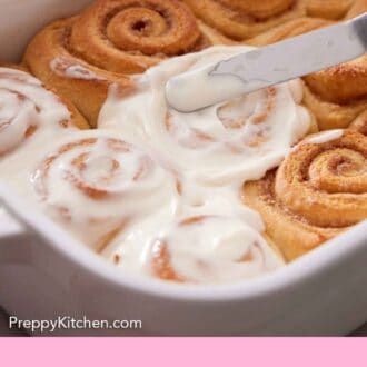 Pinterest graphic of cinnamon rolls in a baking dish getting glazed.