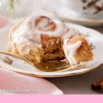 Pinterest graphic of a plate with a cinnamon roll with a fork in front with a bite on it.