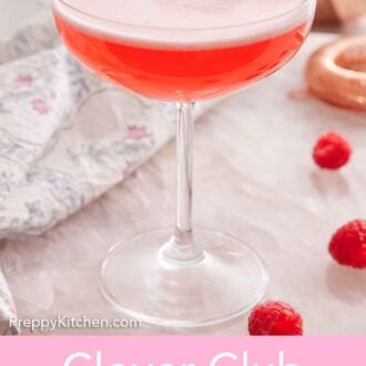 Pinterest graphic of a glass of Clover Club Cocktail with three raspberries as a garnish with more raspberries scattered on the counter.