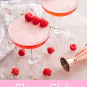 Pinterest graphic of two glasses of Clover Club Cocktail with raspberries as a garnish and on a counter. A jigger and more raspberries scattered on the counter.