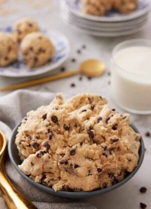 A bowl of edible cookie dough with a glass of milk in the background.