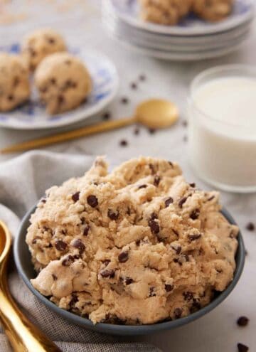 A bowl of edible cookie dough with a glass of milk in the background.