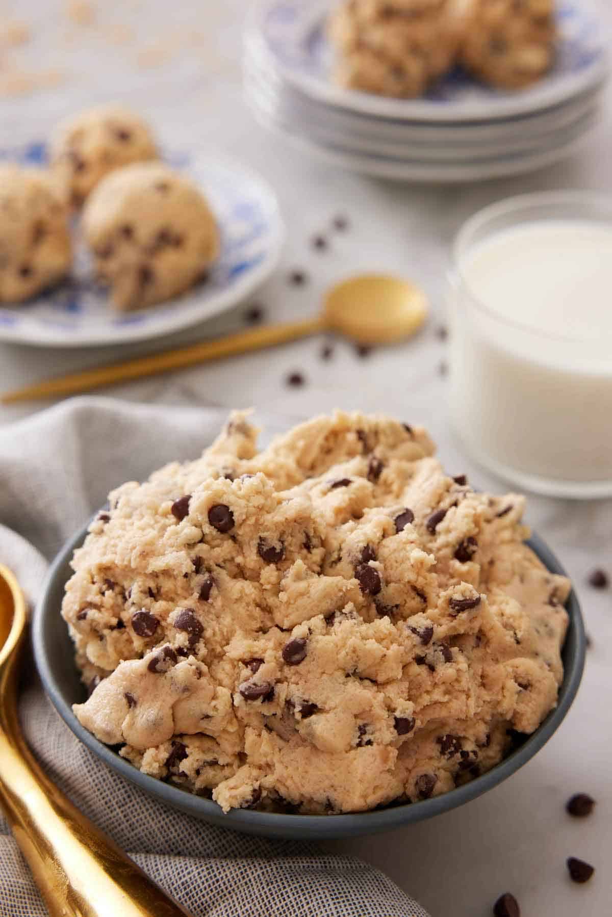 A bowl of edible cookie dough with a glass of milk in the background.