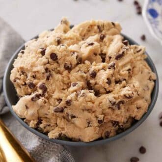 A bowl of edible cookie dough with a plate with scooped servings off to the side along with a scooper.