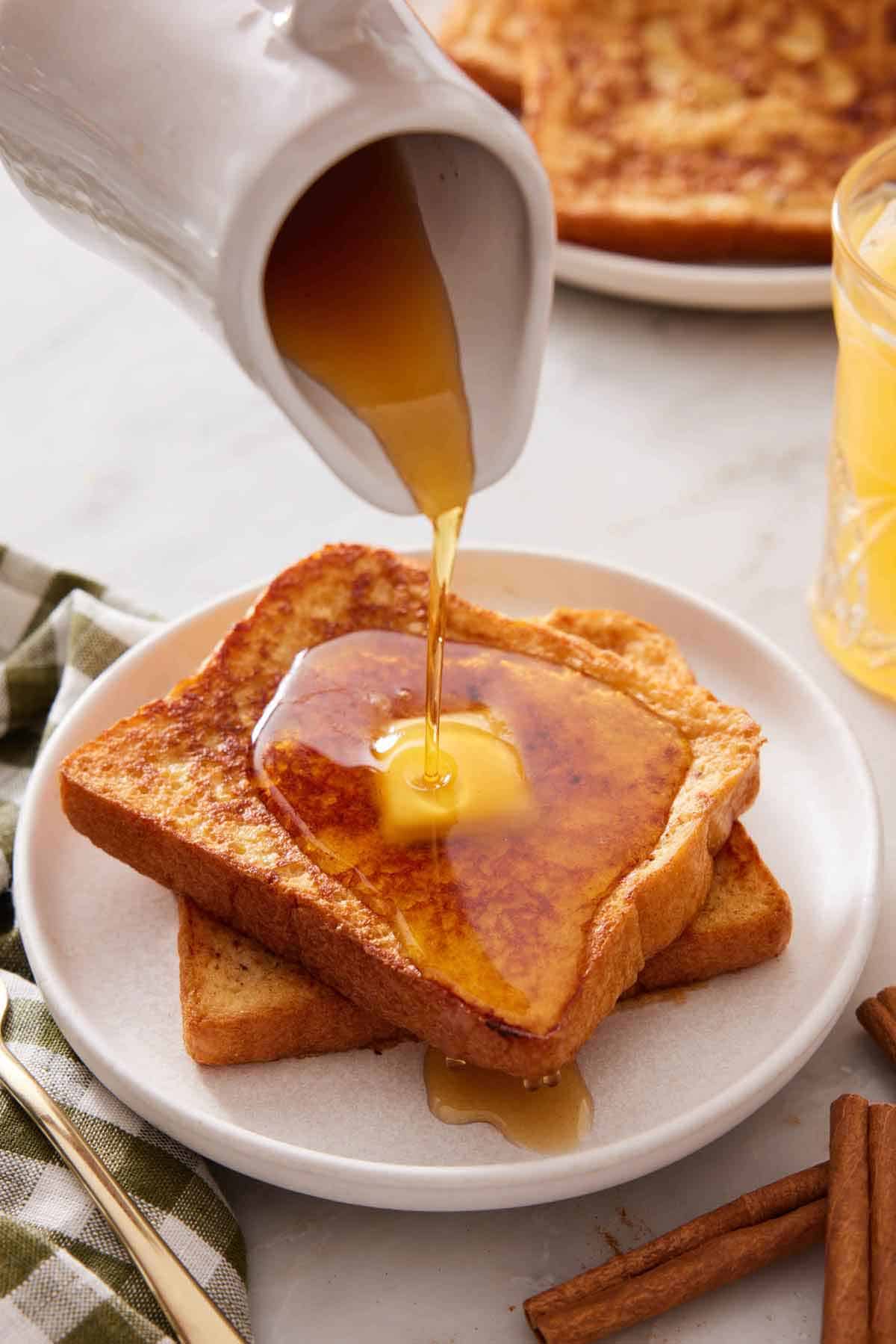 A plate with two pieces of french toast with butter on top with maple syrup poured on top.