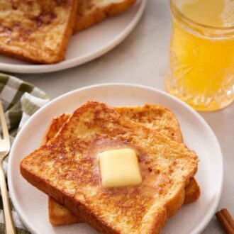 Pinterest graphic of a plate with two pieces of french toast with a knob of butter on top. Orange juice and more french toast in the background.