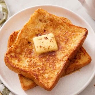 A plate of two french toast with a knob of butter and some cinnamon on top.