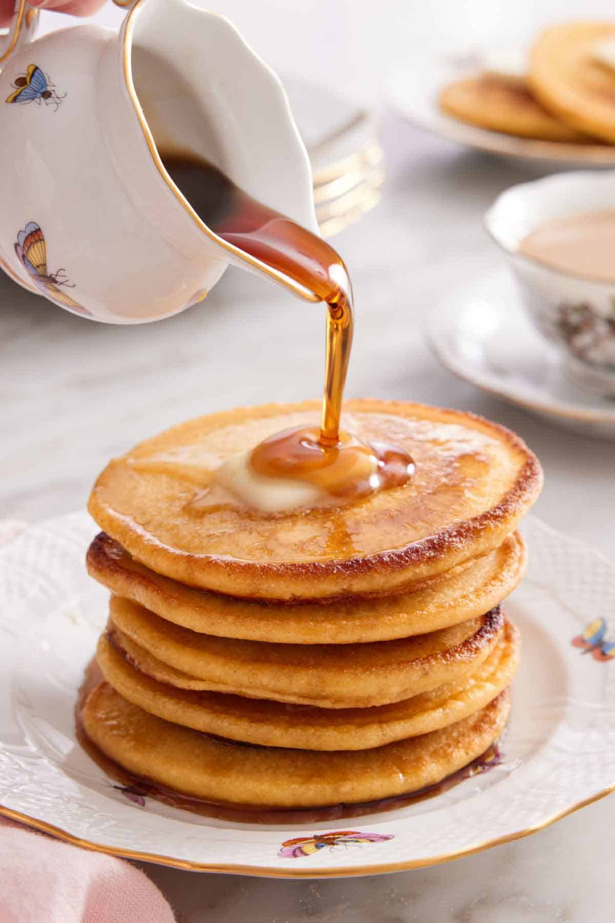 A stack of Johnny cakes with a knob of butter on top and maple syrup poured over top.