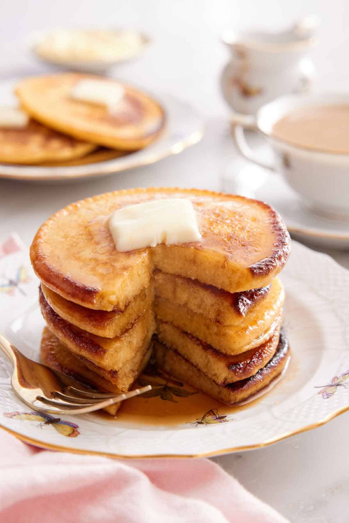 A stack of Johnny cakes with a portion cut out. Butter on top and a fork on the cake.