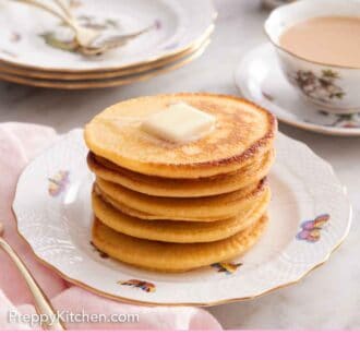 Pinterest graphic of a stack of Johnny cakes with a pat of butter on top and a cup of coffee in the background along with a stack of plates.