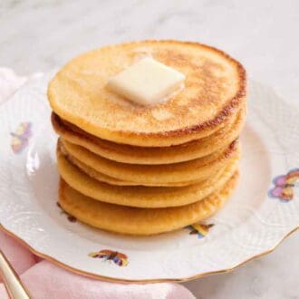 A stack of Johnny cakes with a pat of butter on top with a fork off to the side.
