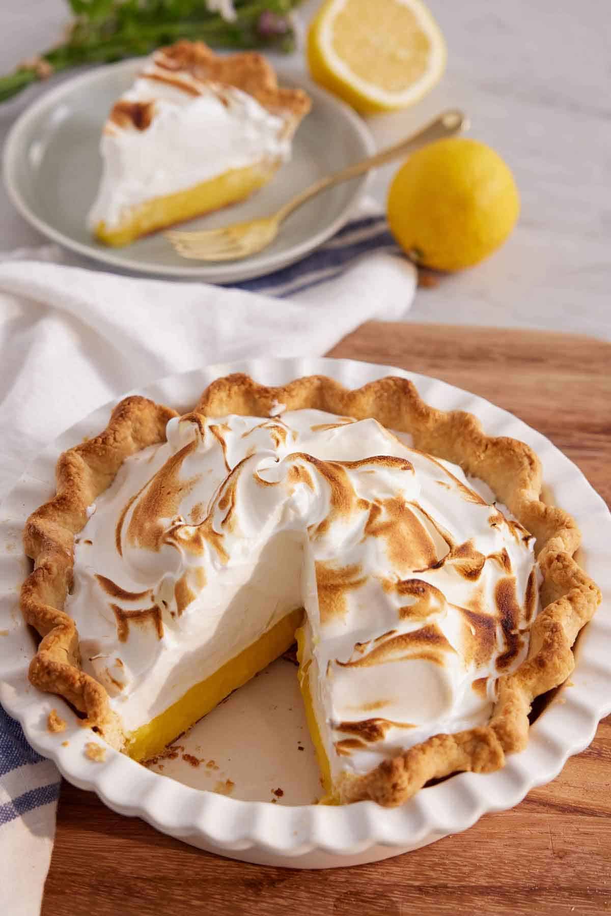 A baking dish with a lemon meringue pie inside with one slice cut out.