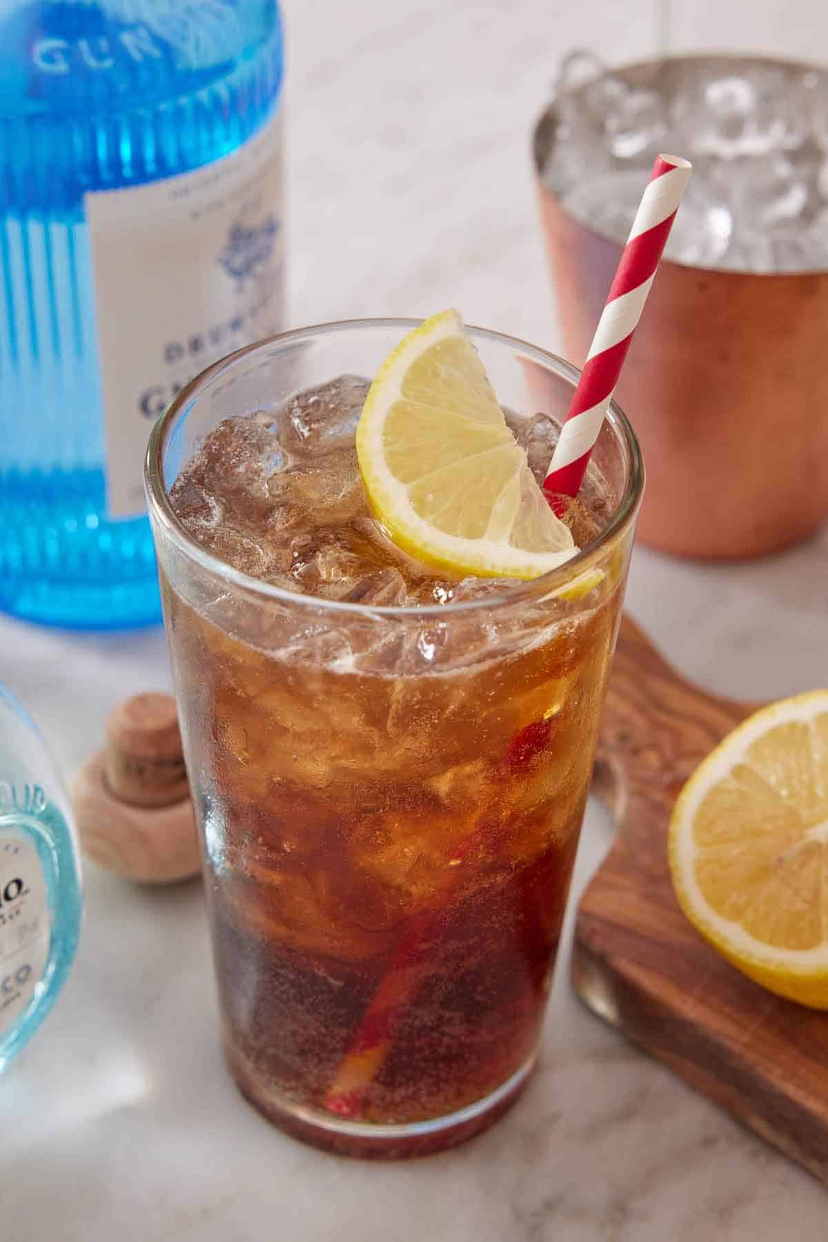 A glass of Long Island Iced Tea with a slice of lemon and a striped straw.