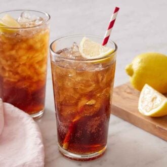 Two glasses of Long Island Iced Tea with cut lemon in the background on a wooden cutting board.