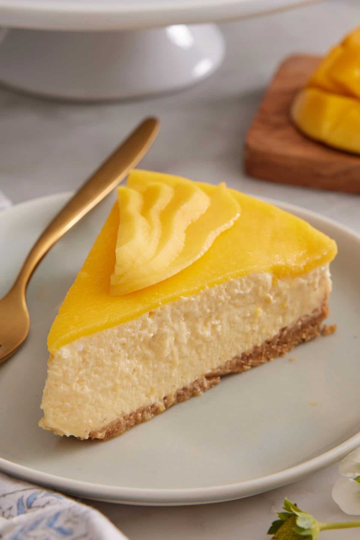 A slice of mango cheesecake on a plate with sliced mango on top.