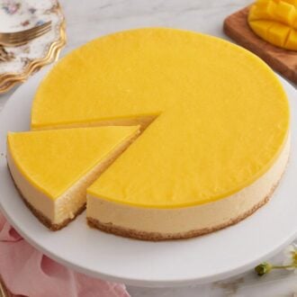 A mango cheesecake on a cake stand with a slice cut and slightly pulled out.