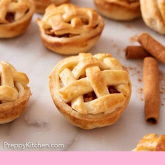Pinterest graphic of multiple mini apple pies on a marble surface with cinnamon sticks on the side.
