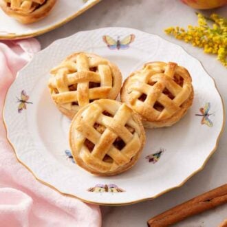 A plate with three mini apple pies with cinnamon stick on the side with some flowers.