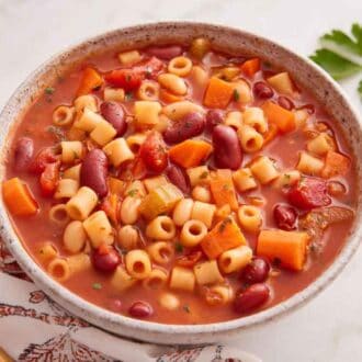 A bowl of pasta fagioli with a spoon beside it and parlsey to the right.
