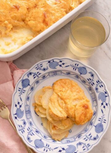 An overhead view of a plate of potatoes au gratin with a glass of wine being it along with a casserole dish.