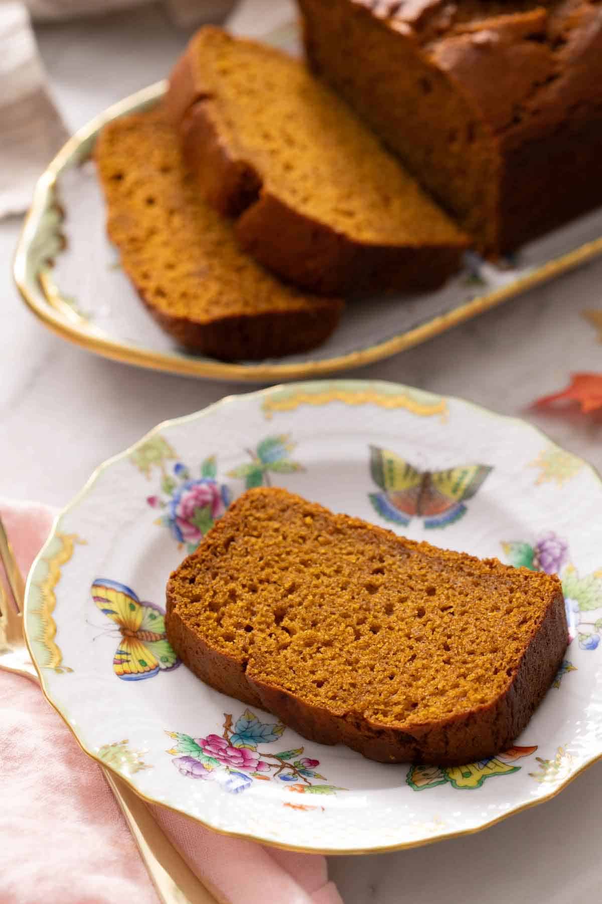 A plate with a slice of pumpkin bread with more in the background.