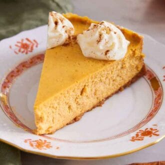 A slice of pumpkin cheesecake with whipped cream and pumpkin pie spice on top.