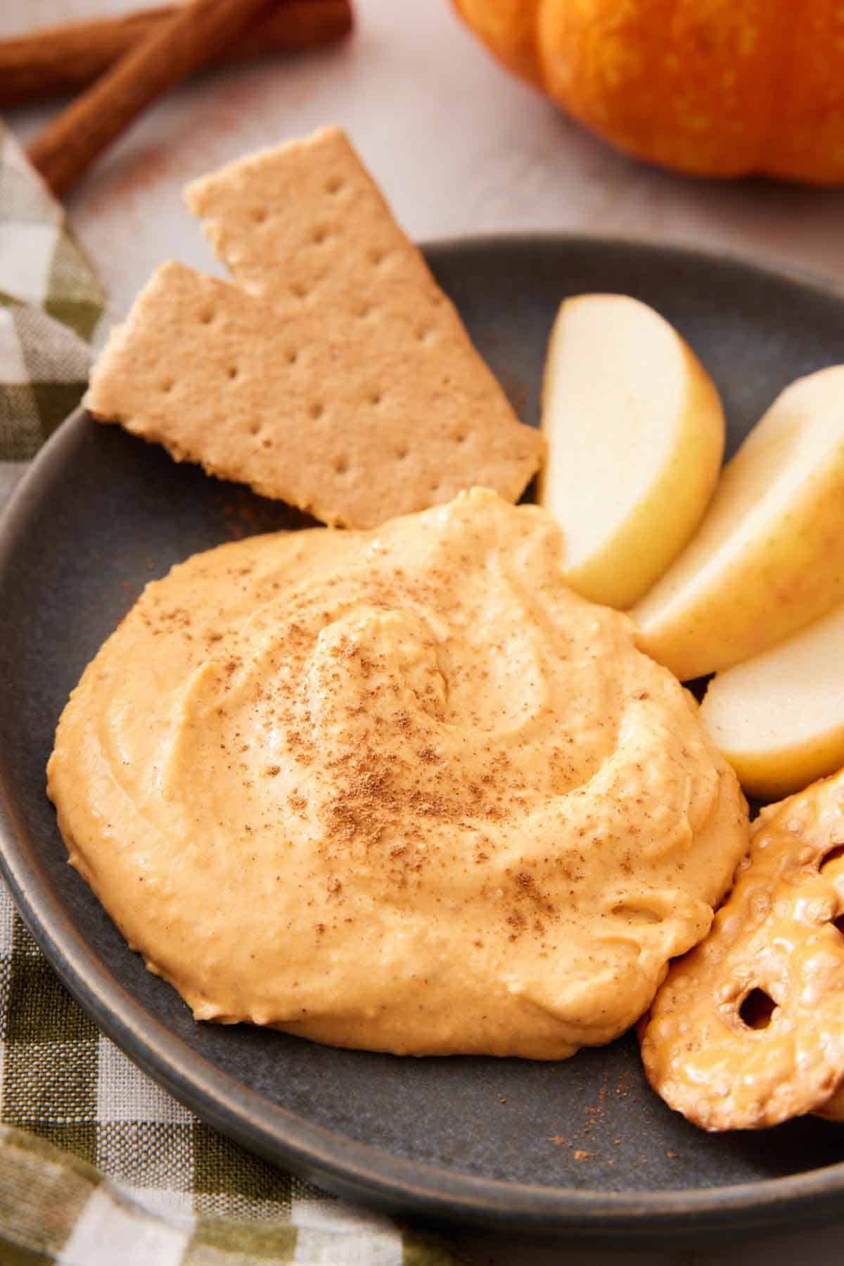 A plate with a dollop of pumpkin dip with crackers and apple slices.