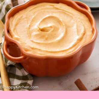 Pinterest graphic of a pumpkin-shaped bowl containing pumpkin dip with some plates in the background.