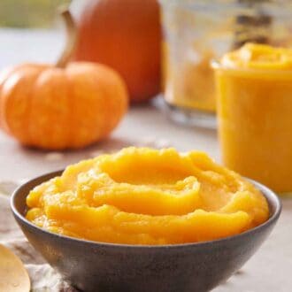 Pinterest graphic of a bowl of pumpkin puree with some pumpkins in the background alongside a food processor bowl and a jar of puree.