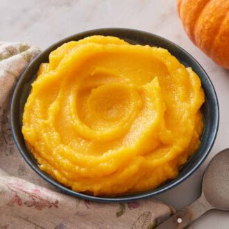A bowl of pumpkin puree with a spoon and pumpkin off the side.