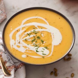 A bowl of pumpkin soup with a drizzle of cream, pepper, and herb garnish.