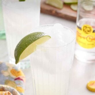 Pinterest graphic of two glasses of ranch water with lime wedges on the rim. A glass of topo chico in the background along with cut limes.