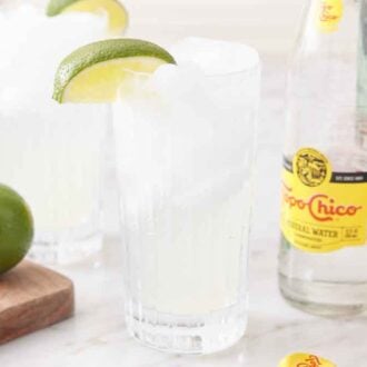 Two glasses of ranch water with a bottle of topo chico and limes on the sides of the drinks.