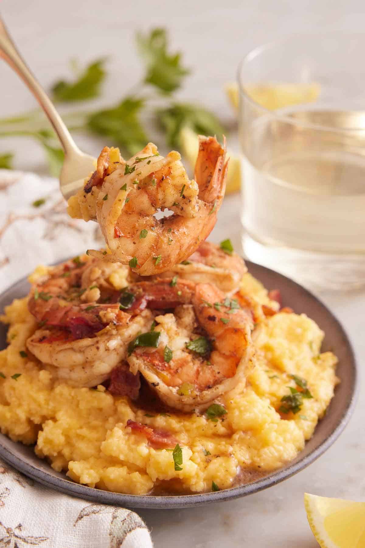 A forkful of shrimp and grits lifted from a bowl with a glass of wine in the background.