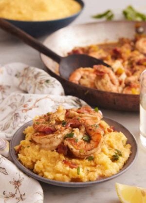 A bowl of shrimp and grits with a skillet of shrimp and bowl of grits in the background.