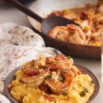 Pinterest graphic of a bowl of shrimp and grits with a skillet of shrimp and bowl of grits in the background.