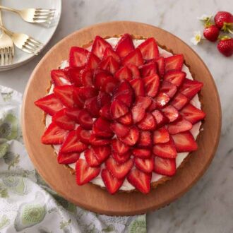 Overhead view of a strawberry tart with a grouping of strawberries on the side and a stack of plates and forks.