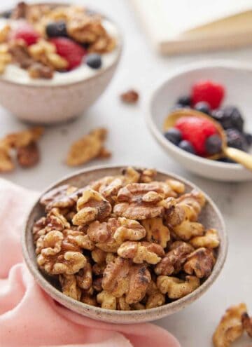 A bowl of toasted walnuts with some berries in the background along with a bowl of yogurt with toasted walnuts and berries.