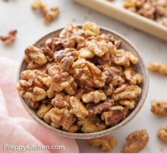 Pinterest graphic of a bowl of toasted walnuts with a sheet pan in the background with more walnuts scattered.
