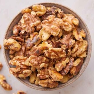 Overhead view of a bowl of toasted walnuts with some scattered around.