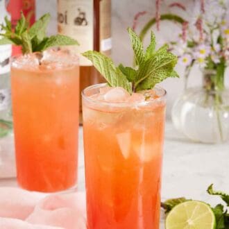 Pinterest graphic of two glasses of zombie cocktail garnished with mint and a cut lime beside the glasses. Flowers in the background with bottles of alochol.